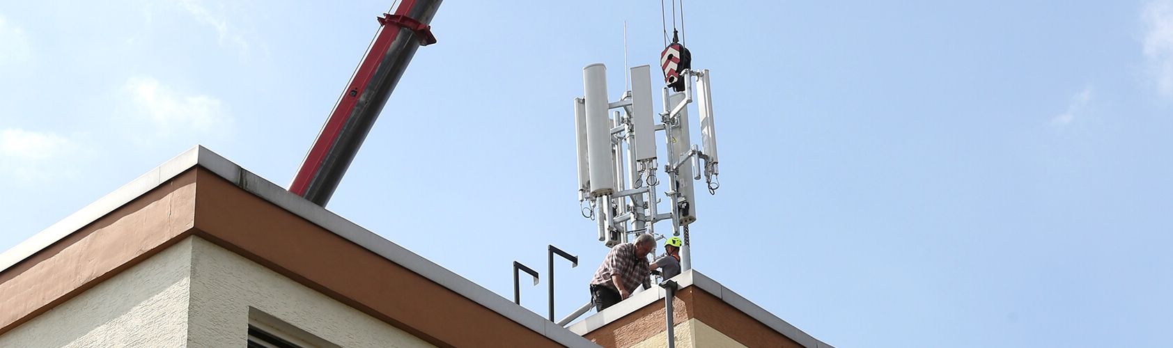 Techniker bauen Mobilfunkantennen auf einem Hausdach auf