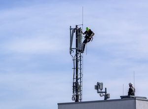 Techniker bauen einen 5G Standort auf einem Hausdach auf.